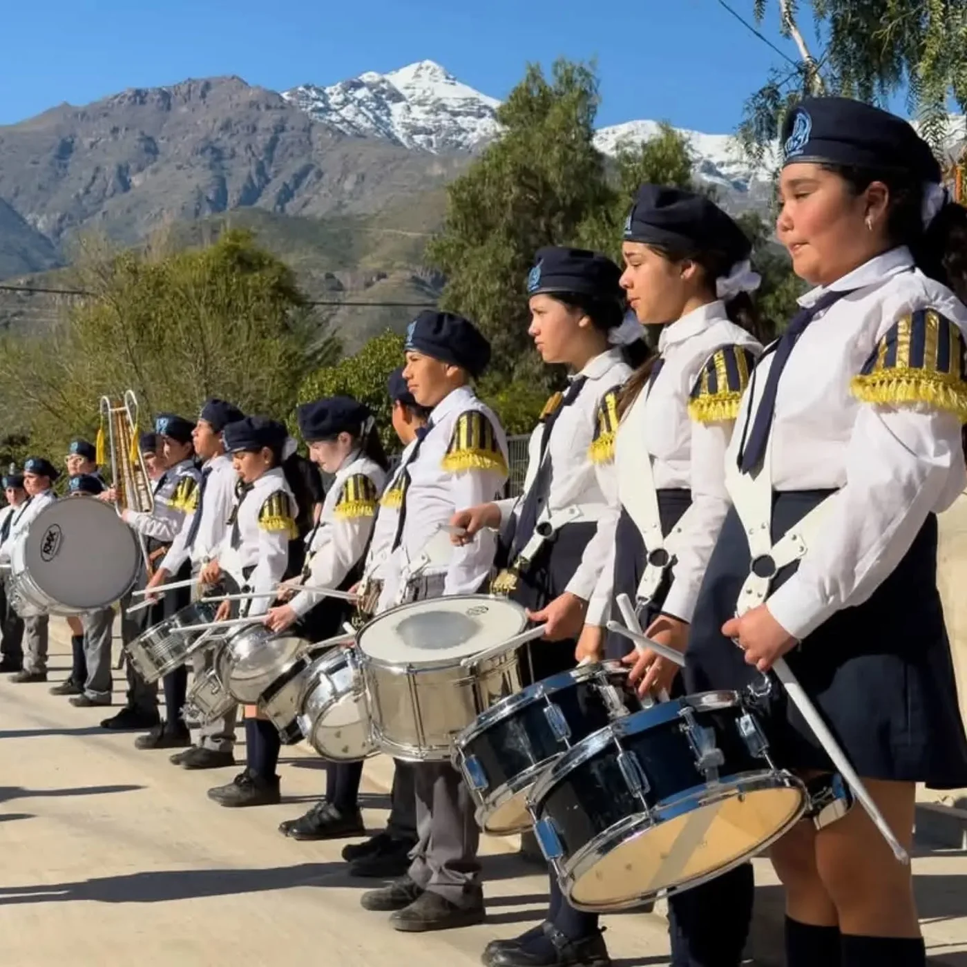 Integrantes de la banda escolar con tambores, con montañas al fondo